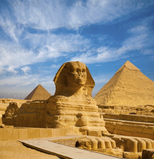 Full profile of Great Sphinx including pyramids of Menkaure and Khafre in the background on a clear