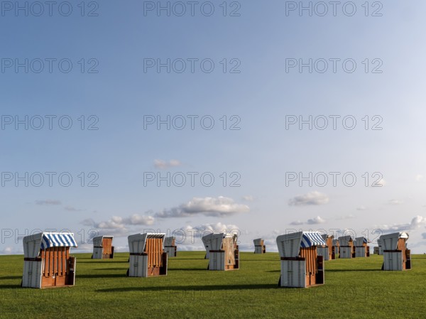 White beach chairs on a meadow and blue sky with clouds in the background, along the coast of the