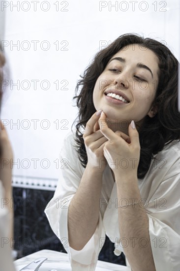 Portrait of a happy woman removing pimples and blackheads from her face in front of the mirror at