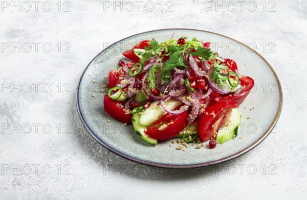Georgian vegetable salad, cucumbers with tomatoes, greens, walnuts, pomegranate seeds, on a light