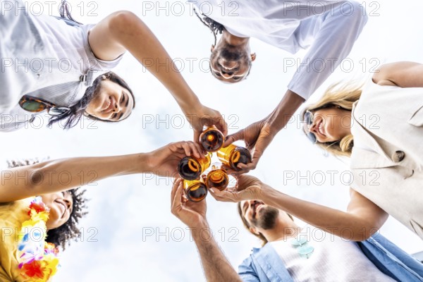 Group of cheerful multi ethnic friends toasting with beer bottles, enjoying a summer beach party
