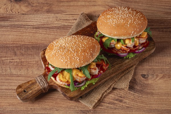 Two shrimp burgers and buns with sesame seeds, bacon, lettuce, tomatoes and onions, on a wooden