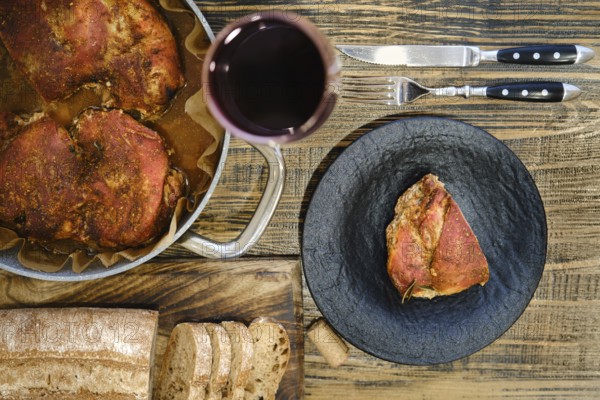 Overhead view of roasted meatin a plate and baking pan served with freshly sliced bread and a glass