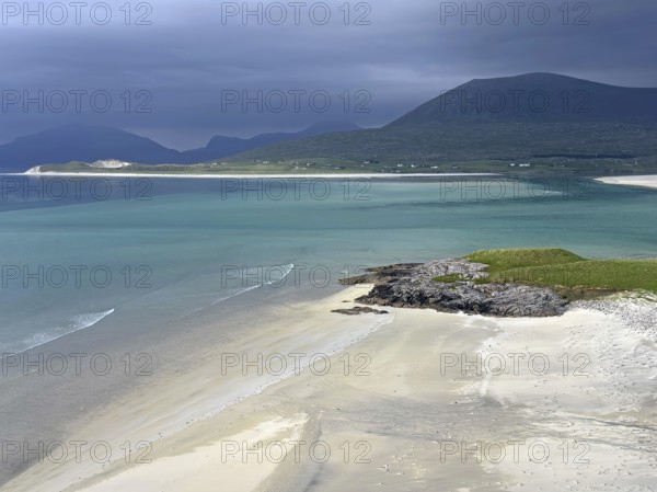Dramatic sky over a calm beach with turquoise water and mountains in the background, Outer