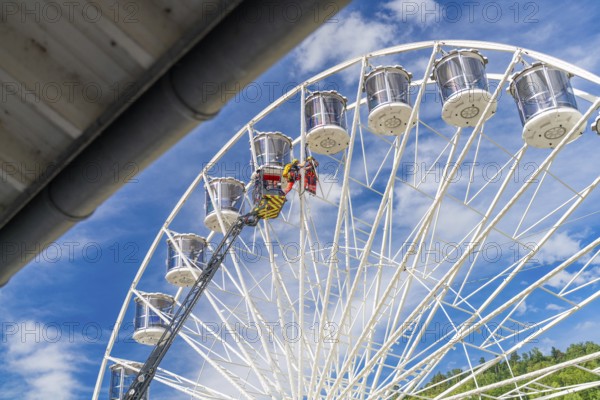 A crane lifts people on a large Ferris wheel up into the blue sky, fire brigade exercise for