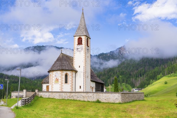 Church with tower and clock, surrounded by meadows and mountains in an alpine landscape, Dolomites,