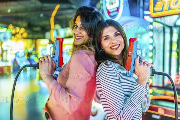 Two joyful women standing back to back, holding toy guns and enjoying playful moments in a vibrant,
