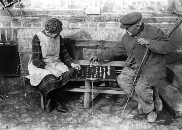 Old man playing chess with girl 1900, Two elderly people playing chess on a bench outdoors,