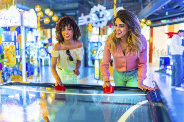 Two female friends enjoying a lively game of air hockey in a vibrant amusement arcade filled with