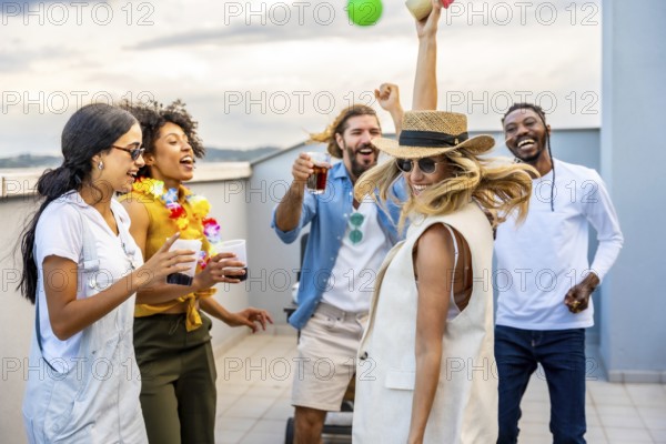 Cheerful multi ethnic friends enjoying cocktails while dancing joyfully at a vibrant rooftop party,