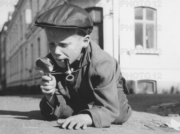 Playing detective. A young boy dressed as a typical looking detective with a magnifying glass and a