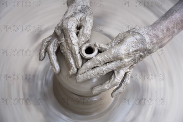 Pottery, artist muddy hands making clay pot giving shape on spinning wheel, semi urban village