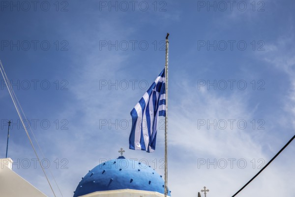 Greek flag waving in the wind, blue church dome, Timios Stavros church, Perissa, Santorini island,