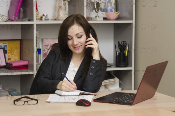 Business woman writing in a notebook and talking on phone