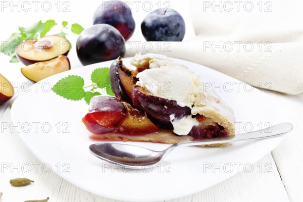 Piece of sweet pie with plum, sugar, cardamom and ice cream in a plate, sprigs of green mint, towel