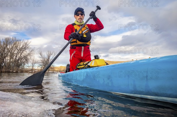 Senior paddler in a dry suit and life jacket is training on stand up paddleboard on a mountain lake
