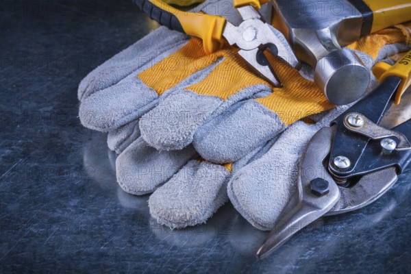 Protective gloves with claw hammer pliers and tin snips on scratched vintage metallic background