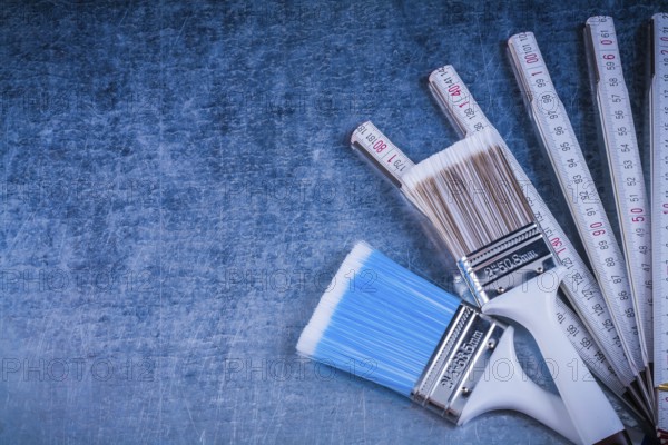 Wooden meter paintbrushes on scratched metallic background construction concept