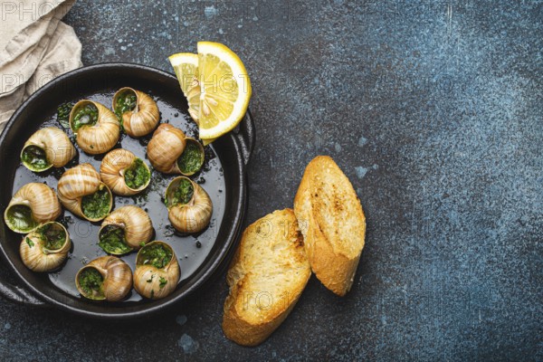 Escargots de Bourgogne Snails with Garlic Butter and Parsley in black cast iron pan with Lemon and