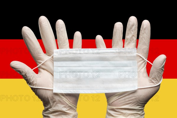 Doctor holding medical face mask in two hands in white gloves on background flag of Germany.