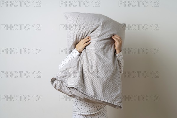Portrait of pretty caucasian girl in white pyjama and pillow in studio white background .