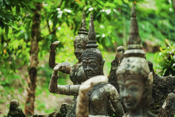 Weathered stone statues amidst green foliage in a forest setting, figures, stone figures,