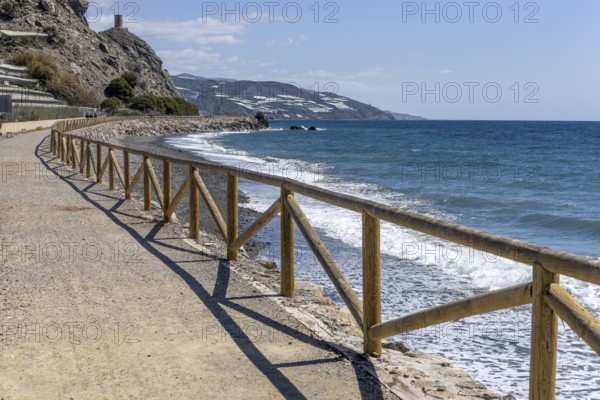 Promenade with wooden railings by the sea in front of the village with blue sky and sea, Castillo