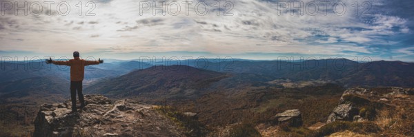 Panoramic view of mountain valley. Young man standing with hands widespread trying to embrace whole