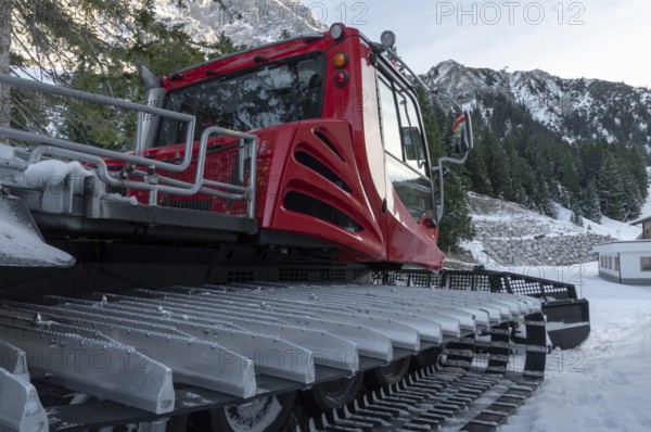 Tracked snow groomer with huge tracks in a winter scenery with the snowy austrian alps and forest