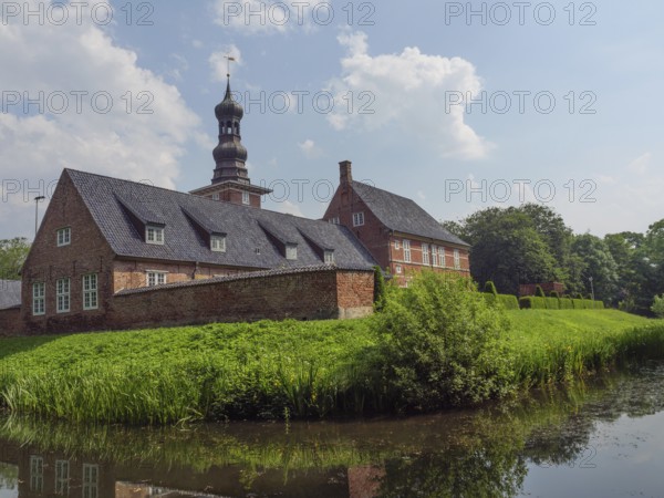 Historic brick building with tower and pond, surrounded by a green garden and blue sky, husum,