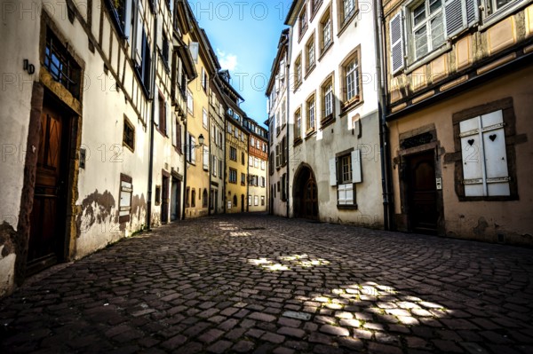 Narrow alley in the old town of Colmar with cobblestones and historic buildings under a blue sky in