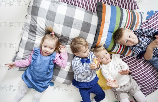 Cute little boys and girls lying on the pillows and playing in the kindergarten, top view