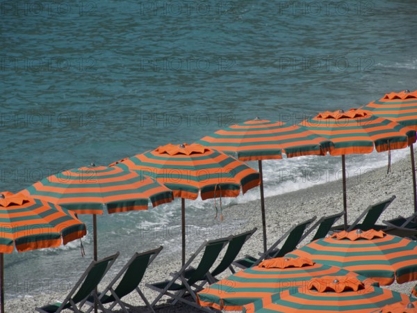 Row of striped parasols on a pebbly beach with a view of the sea and gentle waves, Monte rosso,
