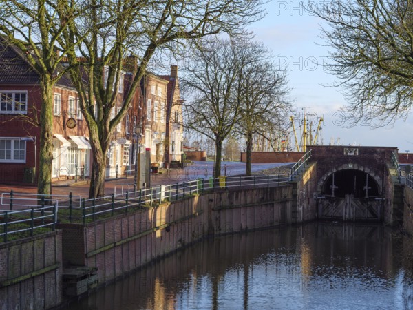Urban scene with canal lined with trees and buildings. Bridge and reflection visible in the water,