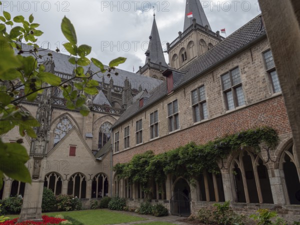 Historic monastery courtyard with Gothic architecture and surrounded by gardens under a cloudy sky,
