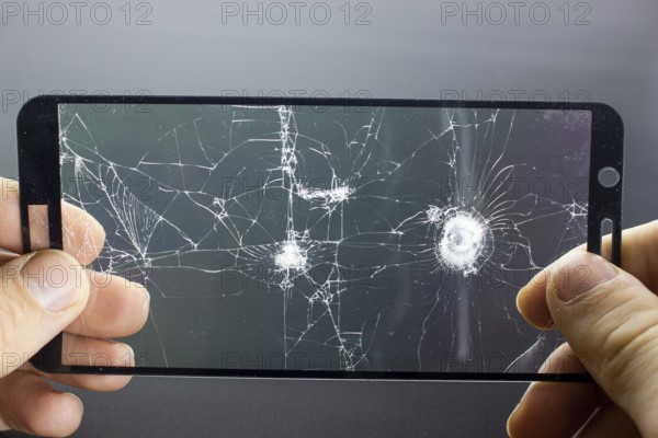 Broken protective glass of smartphone with cracks in hands on black background. Damaged protective