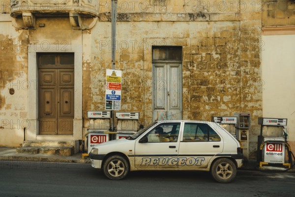 A person refueling a car at a local small gas station located by the side of the road. Self-service