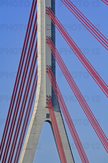 Close-up of red cables supporting a concrete pillar of a modern cable-stayed bridge against a