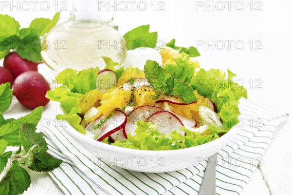 Radish, onion and orange salad with mint, vegetable oil and spices on lettuce in a plate on a towel