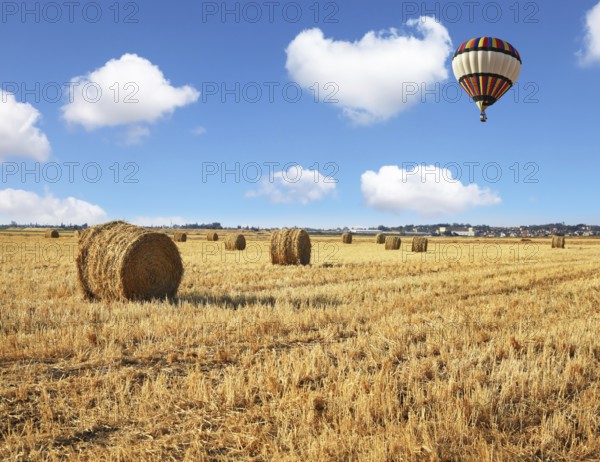 Red and blue balloon slowly floating over kibbutz field. Stacks of harvested wheat beautifully and