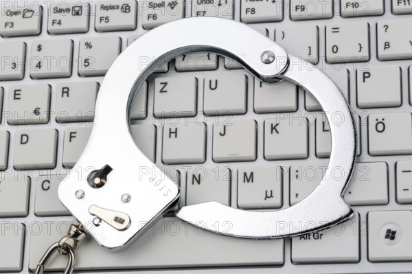 Handcuffs lying on the keyboard of a computer. Symbolic photo for criminality, computer crime and
