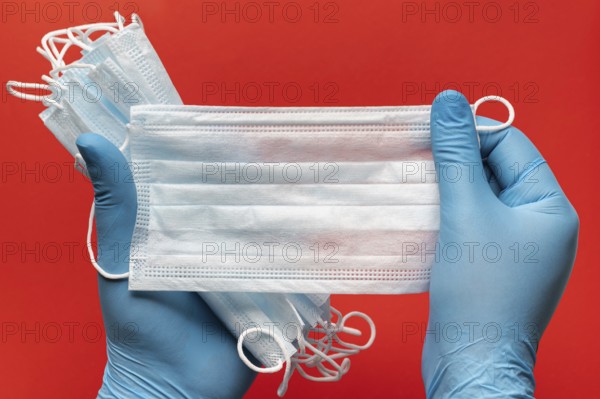 Doctor holds lot respiratory surgical face mask in hands blue medical gloves on red background.