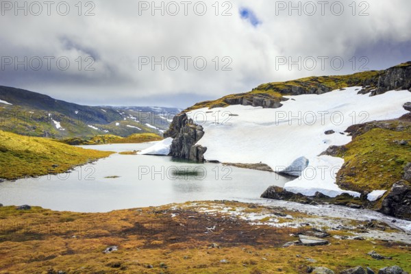 The cold water of the lake is covered with ice floes. Gorgeous Snow Road in Norway. Cold July in