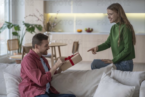 Happy couple celebration. Loving pleased woman gives gift with red tape to smiling husband.