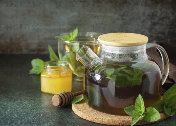 Therapeutic herbal green tea. Hot tea with honey mints in a glass teapot on a stone table. Copy