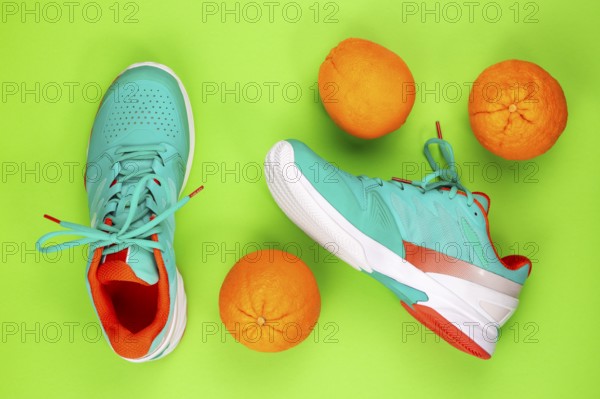 Red, cyan, white pair of new tennis shoes in studio shot over green background with oranges next to