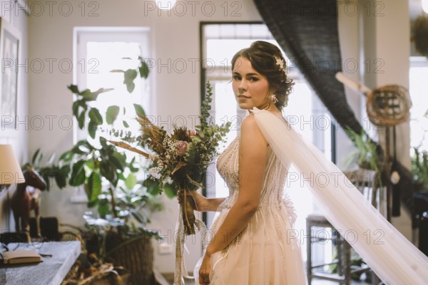 Stylish bride posing at window in light on background. rustic wedding concept. happy bohemian