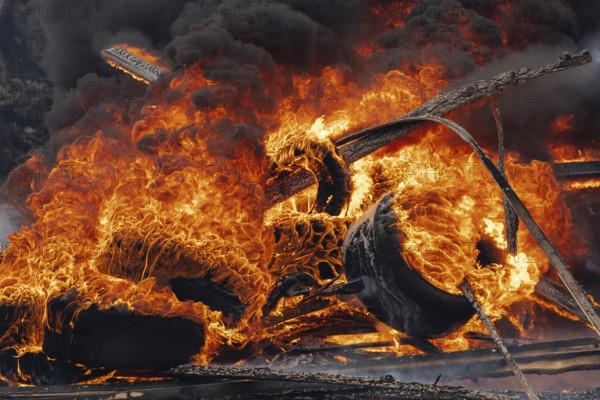 Burning automobile tires, strong flame of red fire and clouds of black fumes in sky. Selective