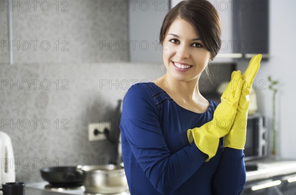 Portrait of young attractive caucasian brunette housewife at kitchen wearing the yellow rubber