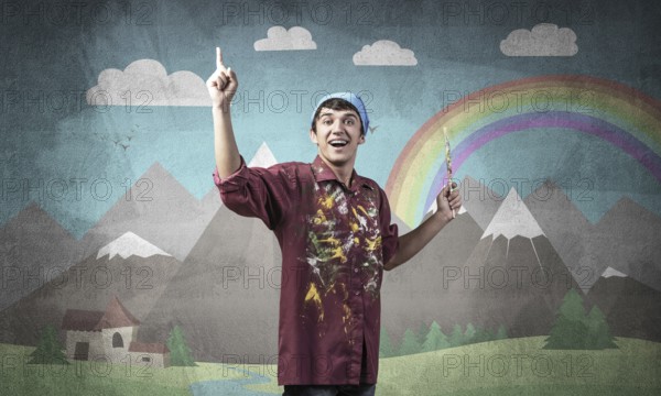 Young male artist with paintbrush. Happy painter in shirt and bandana standing on background